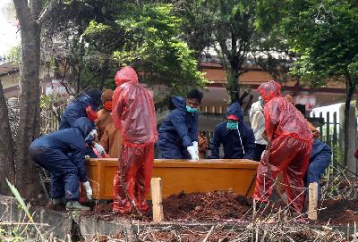Petugas memakai pakaian pelindung dan sebagian lagi memakai jas hujan plastik saat memakamkan jenazah dengan prosedur Covid-19 di pemakaman khusus Cikadut, Bandung, Jawa Barat, Jumat lalu. TEMPO/Prima Mulia