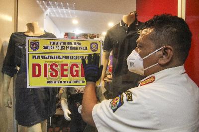 Petugas menempelkan stiker disegel sementara toko pakaian yang masih buka saat PSBB di Depok, Jawa Barat, 19 Mei 2020. ANTARA/Asprilla Dwi Adha