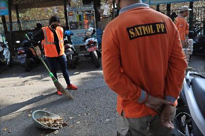 Petugas Satpol PP mengawasi warga yang menjalani hukuman sosial berupa menyapu sampah di Kawasan Pos Polisi Bundaran HI, Jakarta, 26 Juli 2020. TEMPO/Muhammad Hidayat