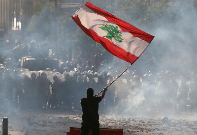 Seorang demonstran mengibarkan bendera Libanon di hadapan polisi dalam bentrokan di Beirut pada Sabtu lalu. REUTERS/Goran Tomasevic 