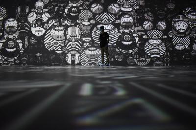 Pengunjung berpose dengan latar video mapping berjudul " Look Into The Eye of Monster" karya kolaborasi Sembilan Matahari dan seniman grafiti  Darbotz  di Kala Kini Nanti Digital Art Space, Bandung, Jawa Barat, 1 Januari 2021. TEMPO/Prima Mulia