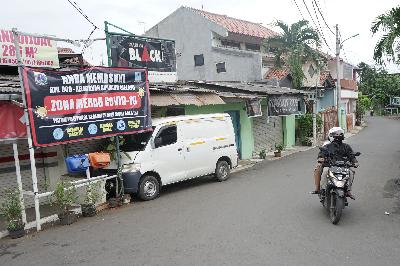 Warga melintas di dekat spanduk pemberitahuan zona merah COVID-19 yang terpasang di Kawasan Cipinang Melayu, Jakarta, 27 Januari 2021. TEMPO/Muhammad Hidayat