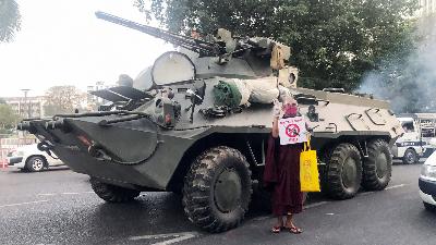 Seorang Biku menunjukan simbol tiga jari di samping kendaraan militer Myanmar, menentang kudeta Militer, di Yangon, Myanmar, 14 februari 2021. Reuters/Stringer