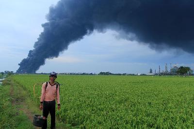 Petani melintas dengan latar asap kebakaran tangki minyak milik Pertamina RU VI Balongan di desa Sukaurip, Balongan, Indramayu, Jawa Barat, 30 Maret 2021. ANTARA/Dedhez Anggara