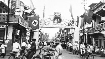 Pintu masuk kawasan Pasar Baru yang dihiasi berbagai bendera, salah satunya bendera dengan lambang Swastika Nazi, di Jakarta, Januari 1937. Tropen Museum