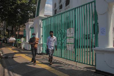 Dua orang pria membawa sajadah di depan pintu gerbang Masjid Cut Meutia yang ditutup saat peniadaan Shalat Jumat di Masjid Cut Meutia, Cikini, Jakarta, 25 Juni 2021. TEMPO / Hilman Fathurrahman W
