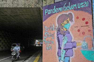 Pengendara melintas di samping mural bertema Covid-19 pada masa Pemberlakuan Pembatasan Kegiatan Masyarakat di kawasan Cikoko, Cawang, Jakarta, 23 Juli 2021. TEMPO / Hilman Fathurrahman W