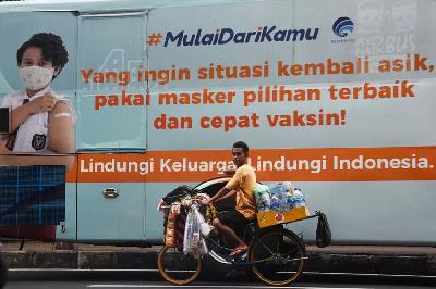 Pedagang melintas di dekat iklan layanan masyarakat tentang imbauan vaksin di kawasan Gambir, Jakarta, 3 Januari 2022.  ANTARA/Indrianto Eko Suwarso