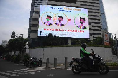 Pengendara motor melintas di dekat layar digital yang menampilkan imbauan protokol kesehatan di Jakarta, 17 Januari 2022. ANTARA/Akbar Nugroho Gumay