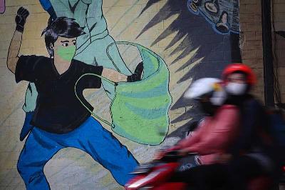 Pengendara melintasi mural bertema Covid-19 di Cikokol, Cawang, Jakarta, 11 Mei 2022. Tempo/Hilman Fathurrahman W