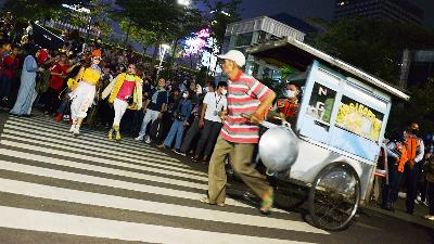 A fried rice merchant passes by as a number of teenagers perform on the Citayam Fashion Week catwalk at the SCBD (Sudirman, Citayam, Bojong Gede and Depok) zebra cross, Dukuh Atas, Jakarta, July 21.
TEMPO/Febri Angga Palguna
