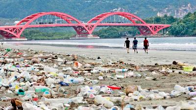 Sejumlah warga melintas di dekat sampah-sampah plastik di pesisir Teluk Youtefa, Jayapura, Papua, Sabtu (23/7/2022).