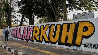 Warga melintas di dekat mural dengan tulisan "Tolak KUHP" di Jalan Pemuda, Rawamangun, Jakarta Timur, Sabtu, 28 September 2019. Mural tersebut menjadi salah satu ungkapan penolakan RUU KUHP yang dinilai kontroversi dan terburu buru. TEMPO/Hilman Fathurrahman W