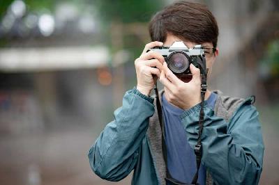 Seorang pria sedang memotret dengan menggunakan kamera tua. Shutterstock