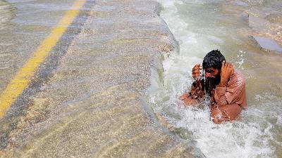 Warga mencoba mendinginkan dirinya di jalan raya yang banjir, setelah hujan dan di Sehwan, Pakistan, September 2022. Reuters/Akhtar Soomro T