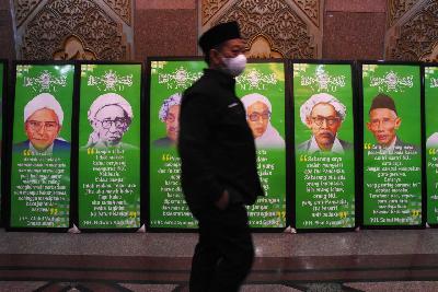 Kader NU melintas di dekat sejumlah foto para tokoh pendiri Nahdlatul Ulama saat diselenggarakannya Rapat Harian Syuriyah dan Harian Tanfidziyah Nahdlatul Ulama di Gedung PBNU, Jakarta, 2021. ANTARA/Indrianto Eko Suwarso