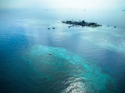 Bidikan drone Pulau Bontosua di Sulawesi Selatan, Indonesia, dengan ribuan m2 terumbu karang yang telah dipulihkan di latar depan. Beberapa struktur reef star yang disusun untuk mengeja huruf HOPE (harapan). Ocean Culture Life