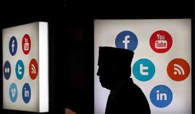 Seseorang melintas di depan papan yang memuat logo platform media sosial di Jakarta, Oktober 2017. REUTERS/Beawiharta