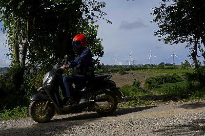 Pengendara sepeda motor melaju dengan latar belakang Pembangkit Listrik Tenaga Bayu (PLTB) Sidenreng Rappang (Sidrap), Sulawesi Selatan, 6 Mei 2024. ANTARA/Hasrul Said